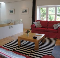 A living room with red sofas a wooden coffee table and glass doors leading outside at The Gallery in Aveton Gifford
