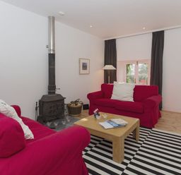 A living room with two red sofas a wooden coffee table a striped rug and a wood burning stove at The Gallery in Aveton Gifford