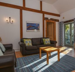 A living room with two leather sofas a wooden coffee table a rug wall beams framed artwork double doors and a television on a stand at Bradbridge Barn in Newton Ferrers