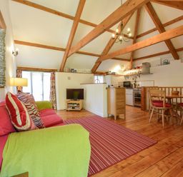 A living room with wooden beams a red sofa a small dining table and a kitchen at Parsonage Farm Cottage in Newton Ferrers