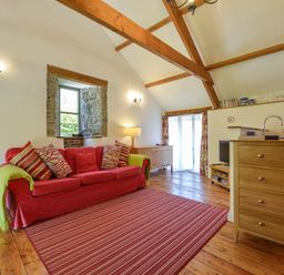 A living room with a red sofa and striped rug at Parsonage Farm Cottage in Newton Ferrers