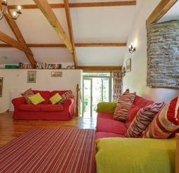 A living room with red sofas and striped cushions a striped rug wooden beams and a stone window at Parsonage Farm Cottage in Newton Ferrers