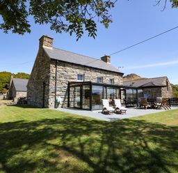 A stone farmhouse with glass sunroom and outdoor patio furniture on a lawn at Garth Morthin The Farmhouse in Porthmadog