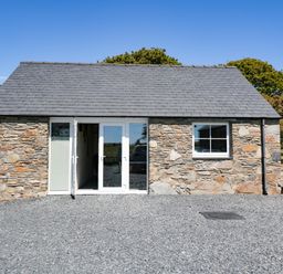 A small stone building with slate roof glass double doors and a window on a gravel ground at Garth Morthin The Farmhouse in Porthmadog
