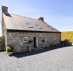 A stone farmhouse with a slate roof and gravel ground outside at Garth Morthin The Farmhouse in Porthmadog