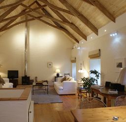 A living room with wooden beams on the ceiling sofas a wood stove and a dining table at The Barn in Aveton Gifford