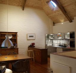 A kitchen and dining area with wooden ceiling beams and furniture at The Barn in Aveton Gifford