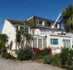 A two story house with a balcony and garden with plants and trees at 3 Tarifa in Bigbury-on-Sea