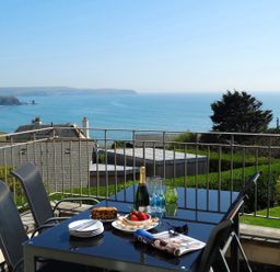 A balcony with a glass table and four chairs overlooking the sea at 3 Tarifa in Bigbury-on-Sea