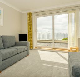 A living room with two gray sofas a small wooden table a TV and large sliding glass doors overlooking a balcony and sea at 3 Tarifa in Bigbury-on-Sea