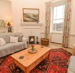 A sitting room with sofas a wooden coffee table a red patterned rug a fireplace and floral curtains at The Bathing House in Ashprington
