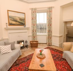 A living room with two sofas and a wooden coffee table in front of a fireplace with a fire burning at The Bathing House in Ashprington