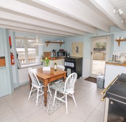 A kitchen with a wooden table and four chairs a window seat stove and door to outside at The Bathing House in Ashprington