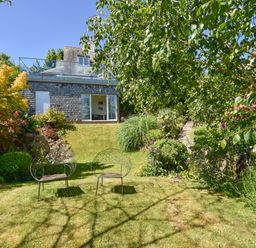 A garden with two metal chairs on grass and a house with a glass door in the background at Dove Cottage in Dittisham
