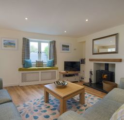 A living room with two sofas a wooden coffee table a fireplace and a window seat at Junket Cottage in Noss Mayo