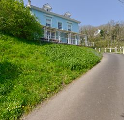 A blue two-story house with white trim on a hill next to a paved driveway and green grass at Woodlands in Dartmouth