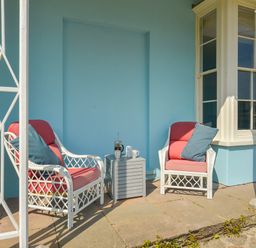 A porch with two white wicker chairs with red cushions and blue pillows and a small gray table with coffee items at Woodlands in Dartmouth