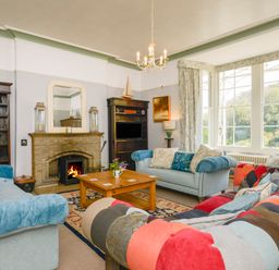A living room with a fireplace three sofas a wooden coffee table and large windows at Woodlands in Dartmouth