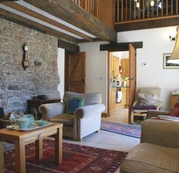 A living room with armchairs a wooden coffee table and a stone wall at The Clock House in Ivybridge