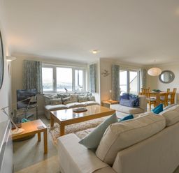 A living room with sofas, a coffee table, a flat screen TV, and a dining table in the background at 13 Burgh Island Causeway in Bigbury-on-Sea