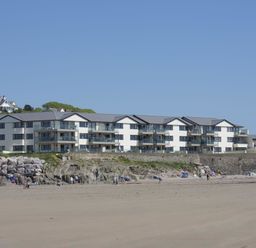 A beach with people and a large apartment building behind rocks at 27 Burgh Island Causeway in Bigbury-on-Sea