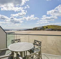 An outdoor balcony with a round table and four chairs overlooking a sandy beach and a distant hill at 24 Burgh Island Causeway in Bigbury-on-Sea