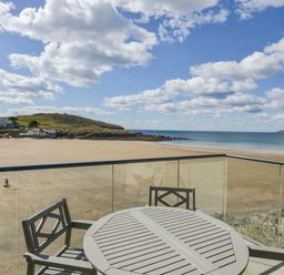 A balcony with a round table and chairs overlooking a sandy beach and the sea at 24 Burgh Island Causeway in Bigbury-on-Sea