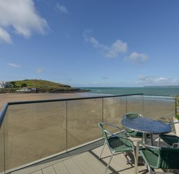 A balcony with a round table and four chairs overlooking a beach and an island at 23 Burgh Island Causeway in Bigbury-on-Sea