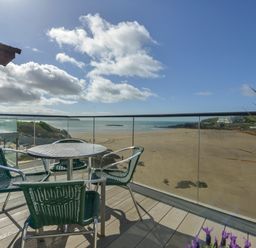 A balcony with a round table and four chairs overlooking a sandy beach and sea at 23 Burgh Island Causeway in Bigbury-on-Sea