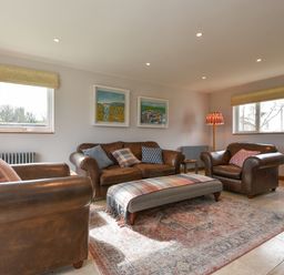 A living room with brown leather sofas a patterned ottoman and paintings on the wall at Orchard View in Kellaton near Hallsands