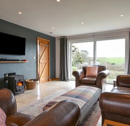 A living room with leather chairs a wood burning stove and large window at Orchard View in Kellaton near Hallsands