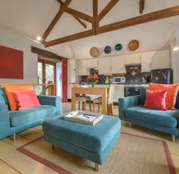 A living area with two blue armchairs and a matching ottoman in front of a wooden dining table and kitchen at Mixit Cottage in Kingsbridge