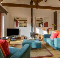 A living room with blue sofas and orange pillows a television and a wood burning stove at Mixit Cottage in Kingsbridge