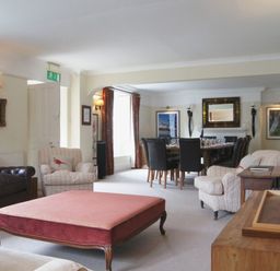 A living room with armchairs and a pink ottoman next to a dining table with black chairs at Maristow Barton in Milton Combe near Lopwell Dam