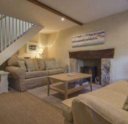 A living room with two sofas a coffee table a fireplace and stairs at Cherry Tree Cottage in Noss Mayo