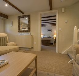 A living room with sofas and a wooden table with a tray leading to a bedroom at Cherry Tree Cottage in Noss Mayo