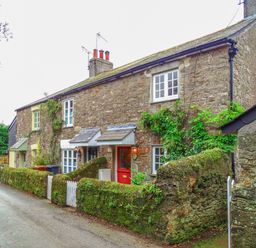 A stone cottage with moss-covered walls and plants along a narrow road at 1 Gabberwell Cottages in Kingston
