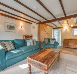 A living room with blue sofas a wooden coffee table and wooden beams on the ceiling at 1 Gabberwell Cottages in Kingston