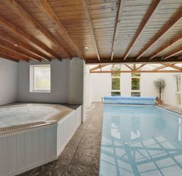 An indoor pool and hot tub with wooden ceiling and windows at Yellowland Farm in Holsworthy