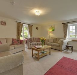A living room with three sofas a wooden coffee table a floor lamp and windows with curtains at Yellowland Farm in Holsworthy