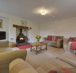 A living room with sofas a wooden coffee table a TV and a lit fireplace at Yellowland Farm in Holsworthy