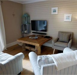 A living room with a wooden coffee table two armchairs a wall-mounted TV and a side table with a lamp at Grandpa Dickson's in Little Petherick