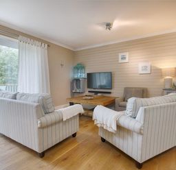 A living room with striped sofas a wooden coffee table and a wall-mounted television at Grandpa Dicksons in Little Petherick