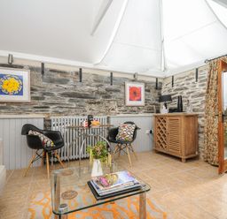 A seating area with two black chairs and a small glass table against a stone wall with framed pictures at Swallow Barn in St Kew
