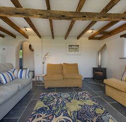 A living room with sofas rug wood burner and exposed ceiling beams at Salty Cottage in Morwenstow