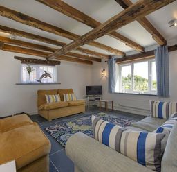 A living room with wooden-beamed ceiling sofas television and a patterned rug at Salty Cottage in Morwenstow
