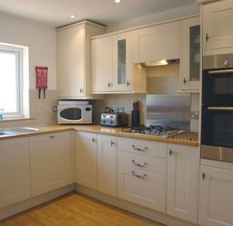A kitchen with white cabinets a microwave toaster gas stove and built in oven at The Loft in Bude