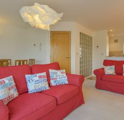 A living room with red sofas and decorative pillows with a wooden dining table behind at The Loft in Bude