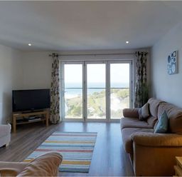 A living room with a sofa a television a striped rug and large glass doors with a view at Seagulls Perch in Mawgan Porth