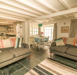 A living room with two grey sofas and a dining table with chairs near windows at Cousham Cottage in Kingsand And Cawsand